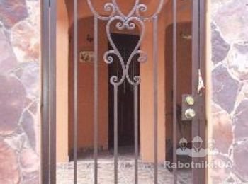Металлическая решетчатая дверь - калитка в заборе из камня.