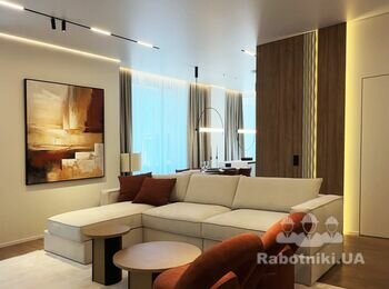 Інтер'єр вітальні після ремонту з бежевим диваном, картиною та трековим освітленням