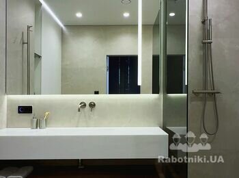 Широка душова з плиткою великого формату, перегородкою з затемненого скла, змішувач золотистого кольору