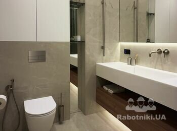 Санвузол із білим литим умивальником, вбудованим в стіну золотистим змішувачем, бежевою плиткою