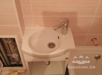 Уложена керамическая плитка, установлен умывальник с тумбой, установлен палстиковый уголок "ванна-стена", герметизация силиконом примыкания умывальник-стена, установлен смеситель и сифон.