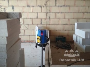 Монтаж внутренних перегородок из газоблока. Для отбивки вертикальной линии используется невелир.