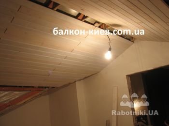 До установки вагонка была покрашена в один слой белой краской (скорее загрунтована). Так как заказчик экономит каждый сантиметр высоты потолка мансарды вагонку приходится собирать вдоль ската крыши и стыки между деревянными панелями оформлять фасками ( на фото видны эти углубления на торцах вагонки) . Фаски фрезеруются вручную. Это увеличивает время монтажа и поднимает цену на обшивку.