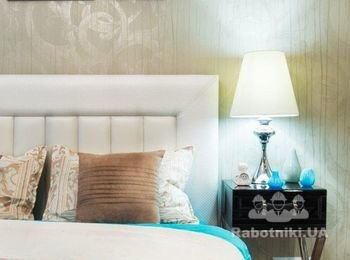 Кровать с кожаным изголовьем молочного цвета гармонирует с абажуром настольной лампы. А основание лампы - с хромированными ножками дизайнерских прикроватных тумб.